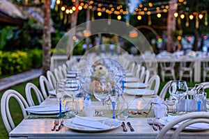 Set table for a white and blue beach wedding dinner decorated with shells, evening lights.