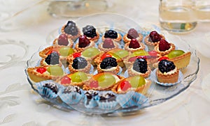 Set of tasty mini cakes with raspberries, blackberries, cranberries, blueberries and grapes on white table. Wedding decoration