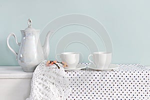 Set of tea cups and ceramic teapot with branch of blossoming cherry on shelf