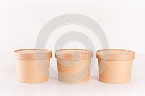 Set of three cardboard bowls with caps for fast food, soup or ice cream on white wood table, food branding identity mockup.