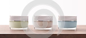 Three closed colored glass jars of cream on wooden table