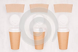 Set of three coffee kraft paper cups with blank label, cap on light wood board, top view.