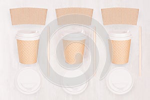 Set of three coffee kraft paper cups with blank label, cap, stick on light wood board, top view.