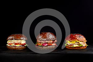 Set of three delicious burgers isolated on a dark background. The concept of fast food, delicious but unwholesome food.