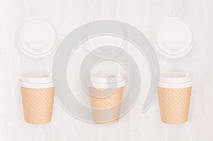 Set of three ribbed coffee kraft paper cups and blank cap on light wood board, top view.