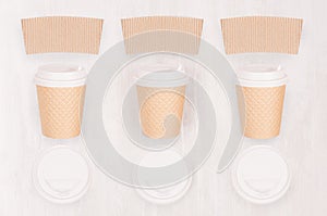 Set of three ribbed coffee kraft paper cups with blank label, cap on light wood board, top view.