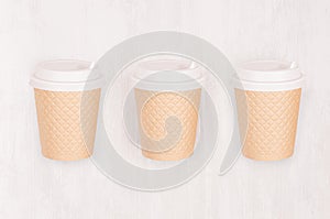 Set of three ribbed coffee kraft paper cups with cap on light wood board, top view.