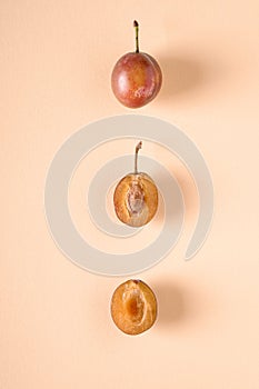 Set of three sliced half ripe sweet plum fruits with water drops on cream colored background, bright, top view, flat lay