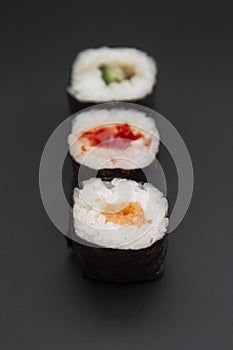 Set of three sushi rolls with fish, avocado and cheese on black background isolated. Traditional japanese food. Asian restaurant