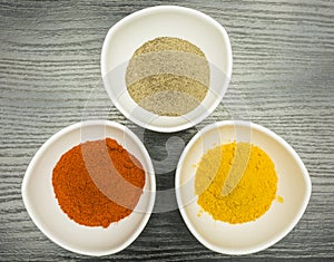 A set of three white bowls with spices - pepper, paprika and curry. View from above.