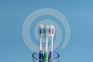 Set of toothbrushes in glass on blue background. Cup with toothbrushes against color background. Dental care