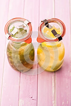 Set of tow summer lemonade with ice and fruit like lemon, lime and mint leaves, summer drink with soda on pink background