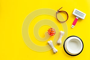 Set of treats and toys for pets with bones, collar and bowl on yellow background top view frame copy space