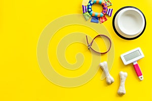 Set of treats and toys for pets with bones, collar and bowl on yellow background top view frame copy space