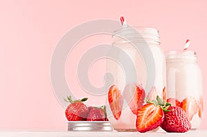 Set of two fresh cold milkshake in hipster jars with cut ripe berries, striped straws in elegance pink kitchen interior.