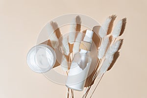 Set of unbranded cosmetic package with face care products. Face cream in open jar and dispencer bottle on beige background