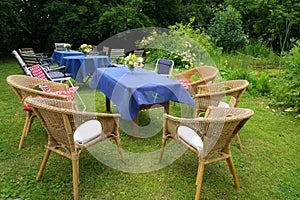 Set up for a casual summer party with tables, blue tablecloths and many different chairs in a rural garden, selected focus