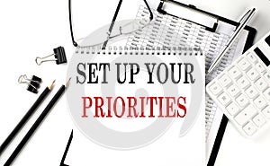 SET UP YOUR PRIORITIES word on notepad with clipboard , chart and calculator, business concept