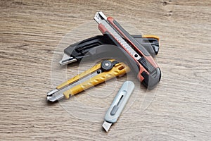 Set of utility knives and box cutters of different colors lying on a wooden surface. Concept of construction tools, office