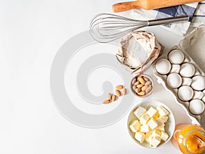 Set of various baking ingredients - flour, eggs, sugar, butter, honey, nuts and kitchen utensils on white background. Top view