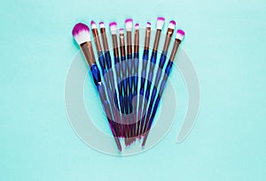 Set of various professional trendy fashion violet purple metallic makeup brushes on pastel green background. Flat lay, top view.