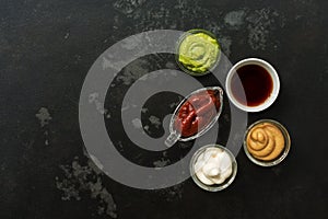 Set of various sauces in bowls on a black stone background. Mustard sauce, tomato, wasabi, mayonnaise, soy. Top view, copy space