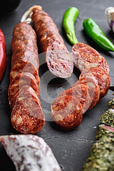 Set of various spanish dry cured salami sausages slices and whole cuts on black textured background