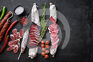 Set of various spanish dry cured salami sausages slices and whole cuts on black textured background with space for text