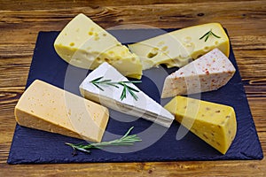 Set of various types of cheese on black slate board on wooden table