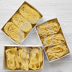 Set of various uncooked pasta in boxes on white wooden background, top view.