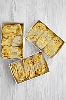 Set of various uncooked pasta in boxes on white wooden surface, top view. Flat lay, overhead, from above