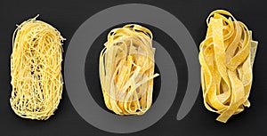 Set of various uncooked pasta: fettuccine, pappardelle, tagliolini on dark black background, overhead view.