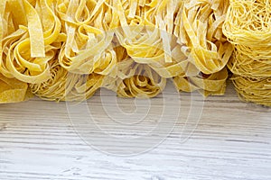 Set of various uncooked pasta over white wooden background.