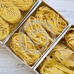 Set of various uncooked pasta in paper boxes on a white wooden background, overhead view. From above, top view, flat lay.