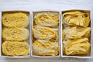 Set of various uncooked pasta in paper boxes on a white wooden surface, top view. From above, overhead.