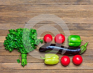 Set of vegetables eggplant, tomatoes, parsley bunch and bell pepper on wooden background, top view close - up