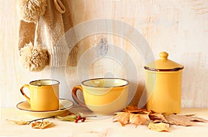 Set of vintage coffee mugs and jar over rustic textured wooden table and autumn leaves. image is retro filtered.