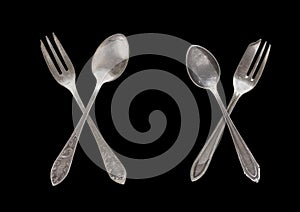 A set of vintage dinnerware: crossed spoons forks and spoons of different shapes and sizes isolated on a black background. Antique