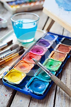 Set of watercolor paints, art brushes, glass of water and easel