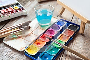 Set of watercolor paints, art brushes, glass of water and easel