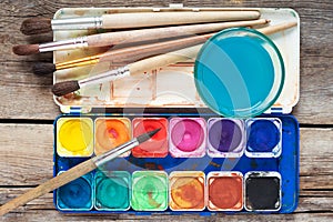 Set of watercolor paints, art brushes and glass of water on old