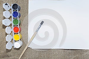 Set of watercolor paints, brushes for painting and blank white paper sheet of sketchbook.