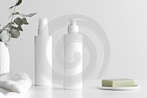 Set of white cosmetic bottles mockup with a towel, natural soap and eucalyptus branches on a white table