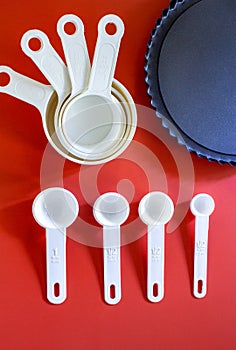 Set of white measuring cups, measuring spoons use in cooking lay on wooden red background with pie mold