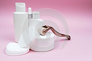 Set of white plastic cosmetic bottles, jar, and derma roller with cotton pads.