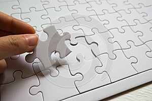 Set of white puzzle pieces and hand holding last one piece