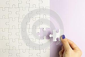 Set of white puzzle pieces and hand holding last one piece on purple background