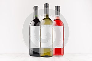 Set wine bottles - red, green, black- with blank white labels on white wooden board, mock up.