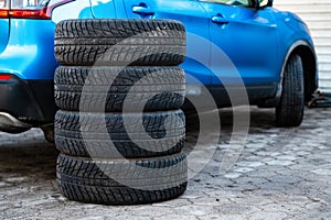 A set of winter tires next to the car in the wheel service, the concept of seasonal tire change