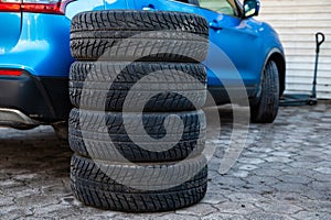 A set of winter tires next to the car in the wheel service, the concept of seasonal tire change